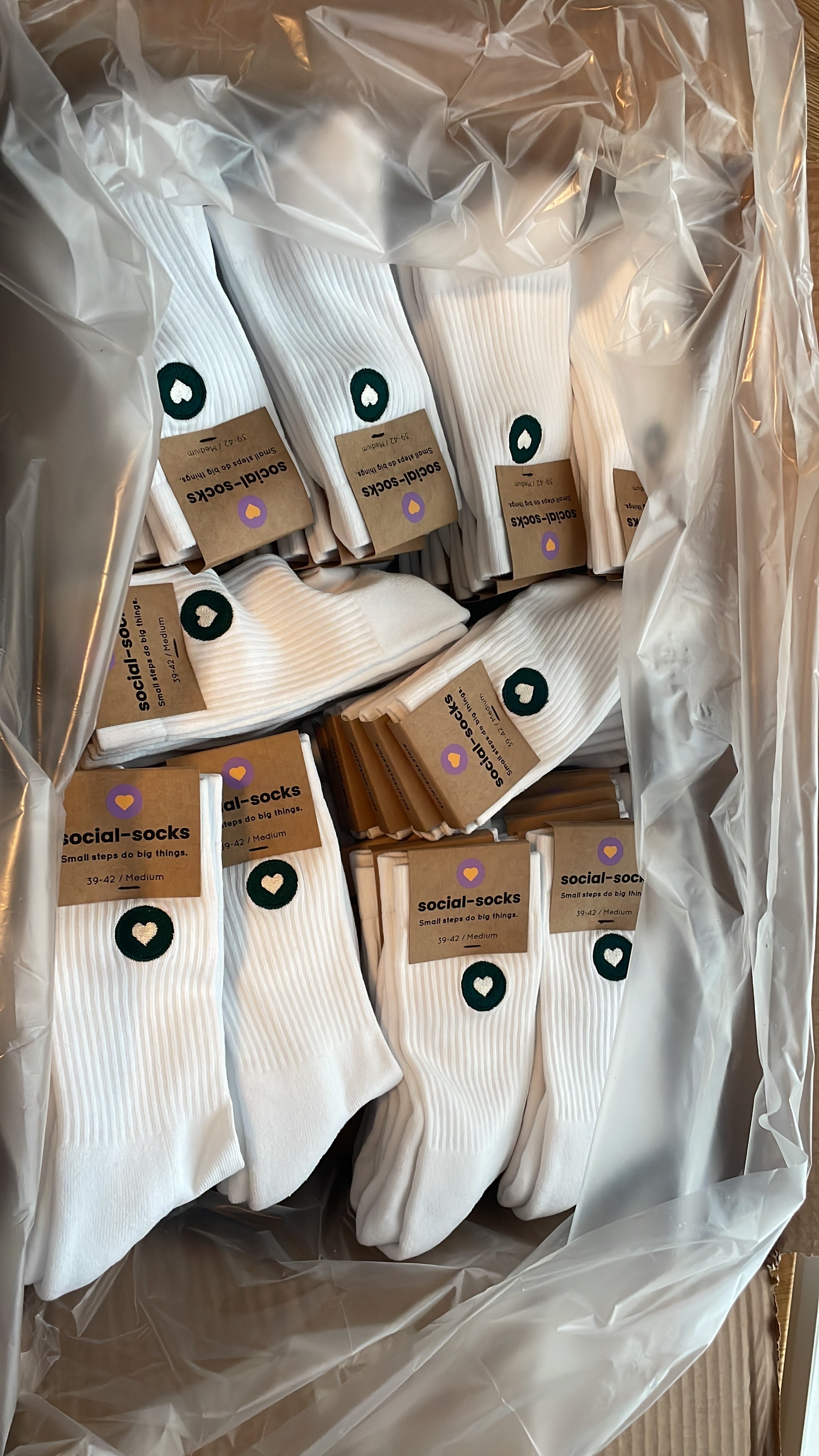 Eine Kiste voller weisser premium Socken aus Bio-Baumwolle mit grünem Herzlogo.