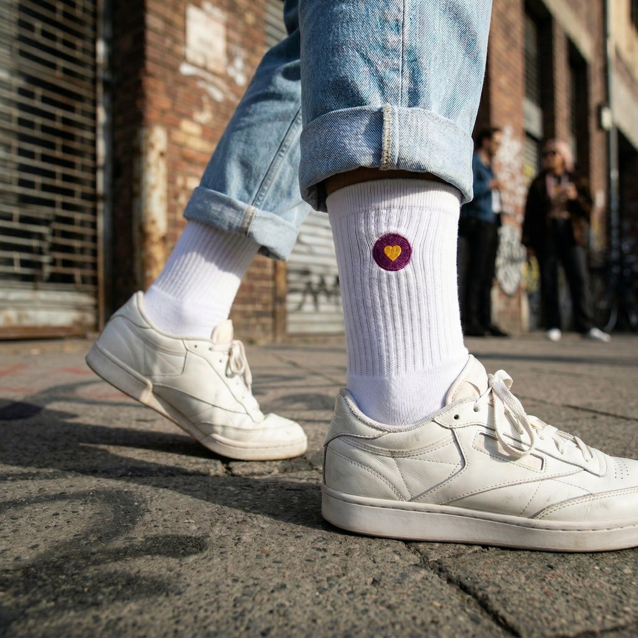 Weisse Premium Socken aus Bio-Baumwolle mit aufgesticktem violettem Herzlogo. Im Hintergrund ist eine Stadt zu sehen.
