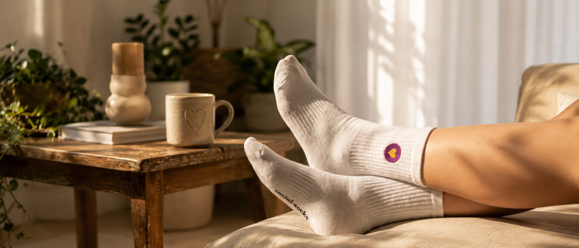 Weisse Premium Socken aus Bio-Baumwolle mit aufgesticktem violettem Herzlogo in einem gemütlichen Wohnzimmer.