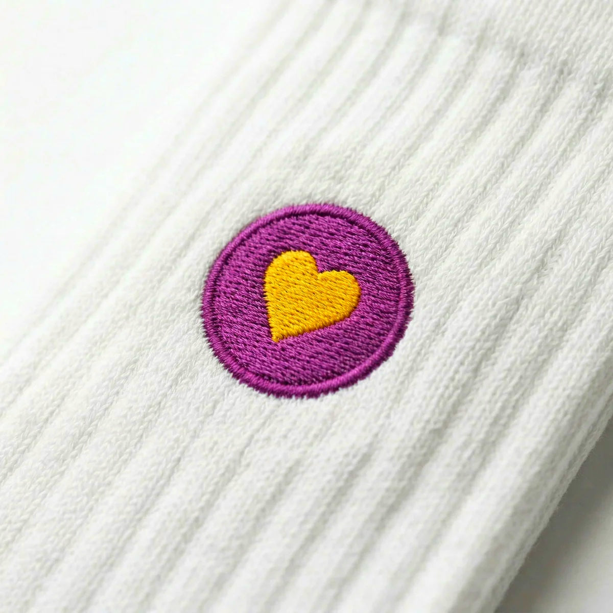 Detailaufnahme einer weissen Premium Socken aus Bio-Baumwolle mit violettem Herzlogo vor weissem Hintergrund.