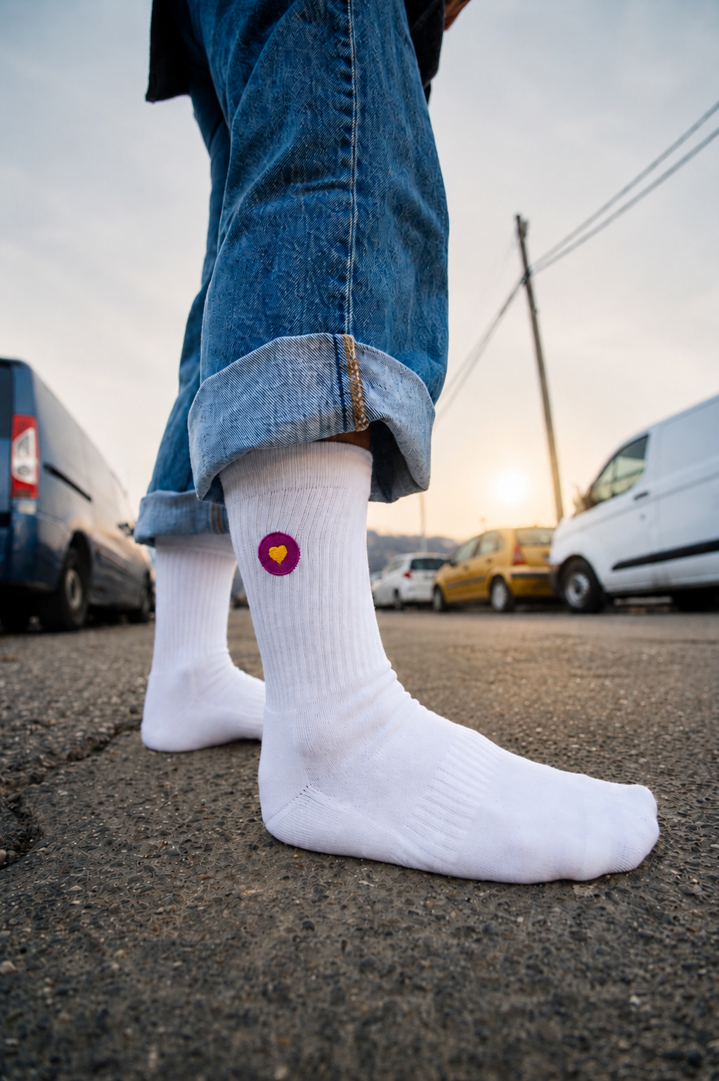 Weisse Premium Socken aus Bio-Baumwolle mit aufgesticktem violettem Herzlogo. Im Hintergrund ist eine urbane Strasse zu sehen.