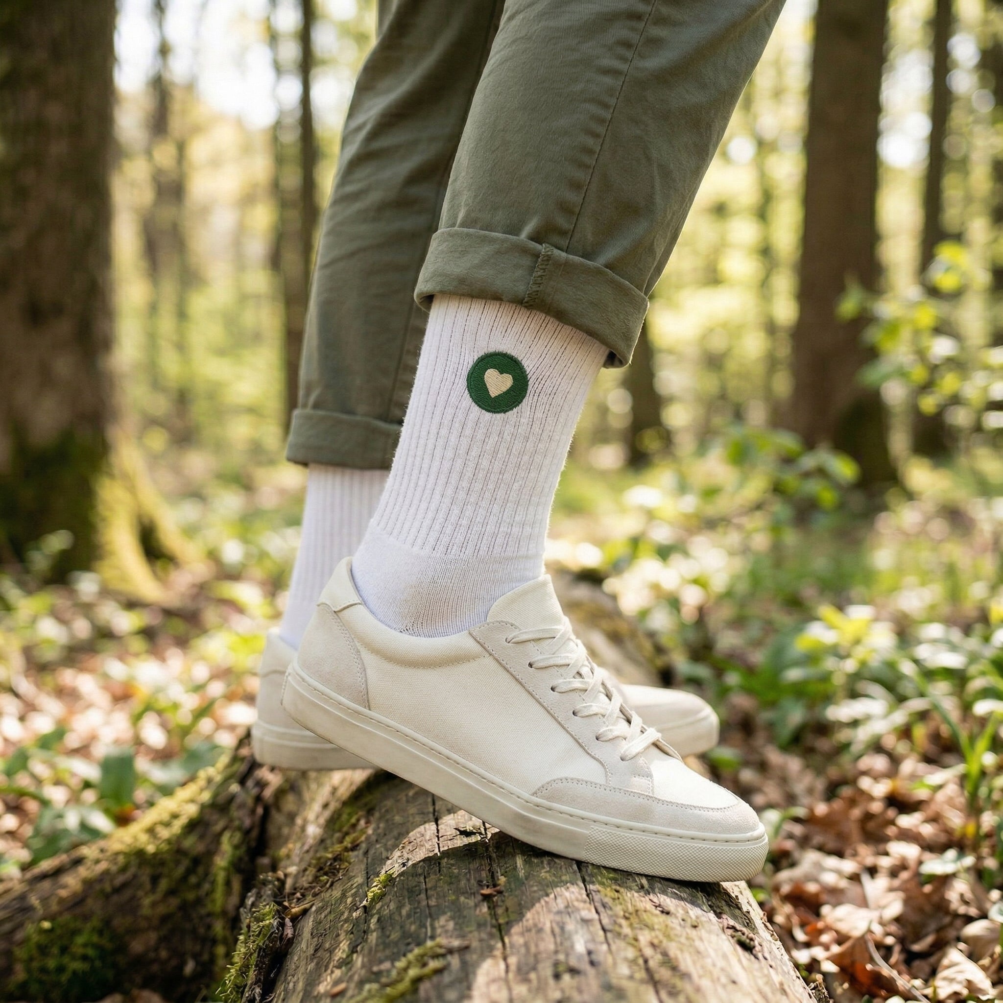 Weisse Premium Socken aus Bio-Baumwolle mit aufgesticktem grünen Herzlogo. Im Hintergrund ist Wald zu sehen.