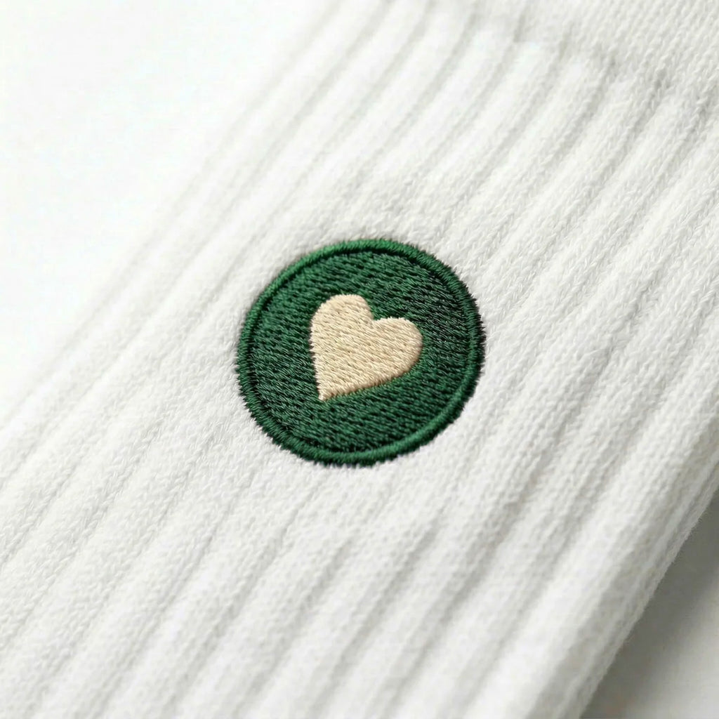 Detailaufnahme einer weissen Premium Socken aus Bio-Baumwolle mit grünem Herzlogo vor weissem Hintergrund.