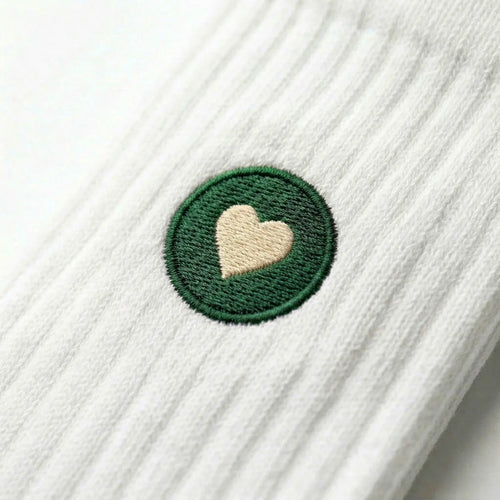Detailaufnahme einer weissen Premium Socken aus Bio-Baumwolle mit grünem Herzlogo vor weissem Hintergrund.